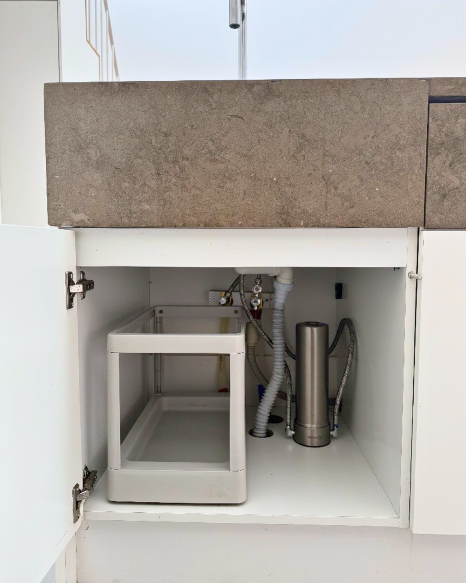 Stainless steel under-sink water filter concept shown through clean filtered water in a modern European kitchen.