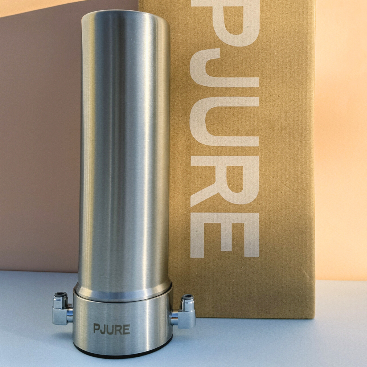 Stainless steel water filter with 'PJURE' branding in front of a brown box with 'PURE' branding.