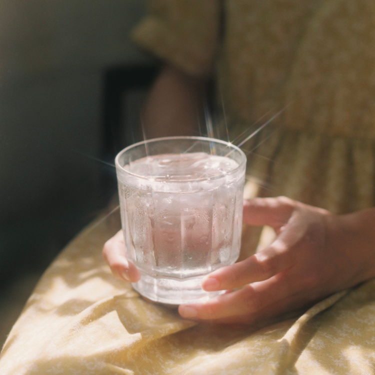 Hand holding a clear glass of water with steam, sitting on a yellow fabric surface.