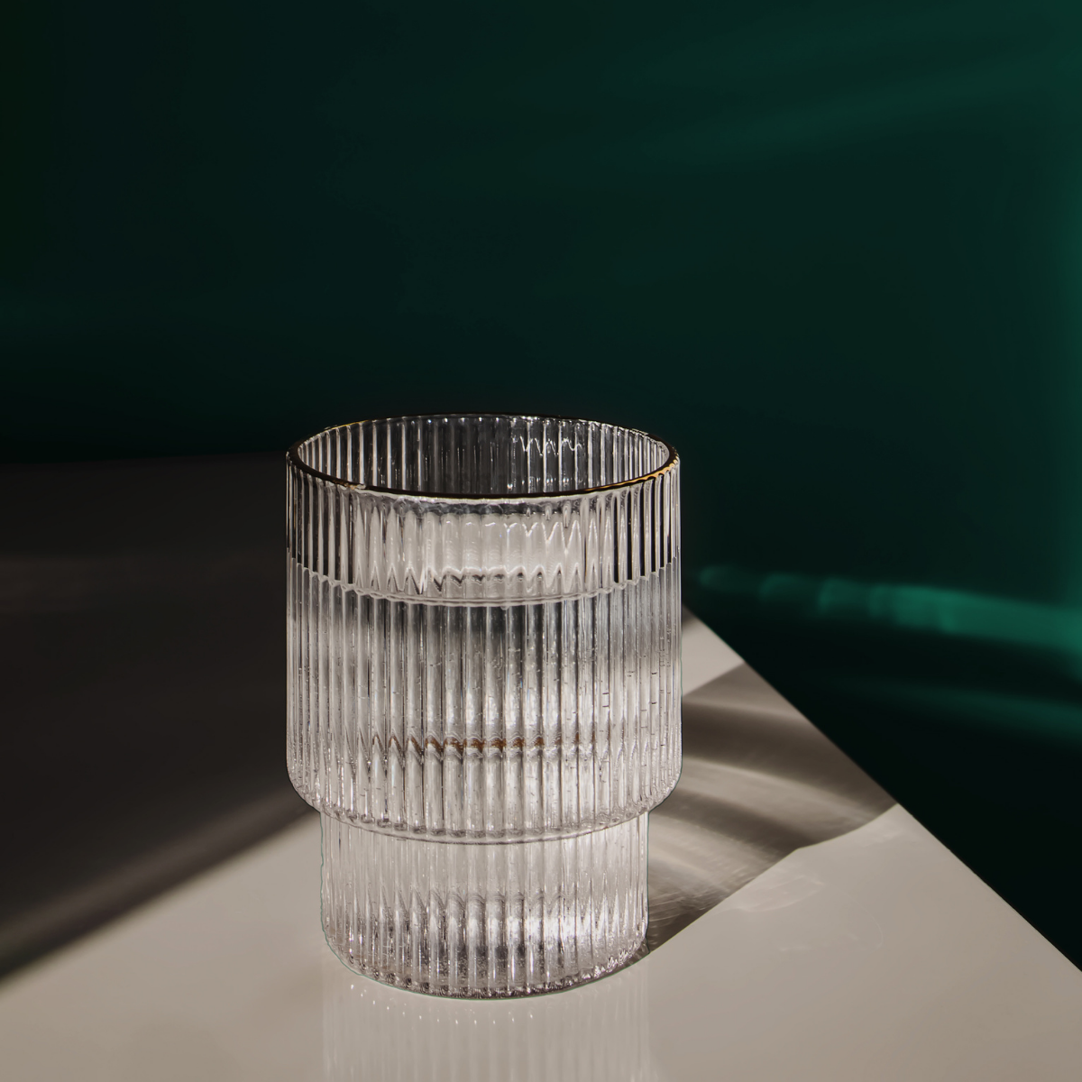 Clear glass vase with ribbed texture on a reflective surface with a dark background